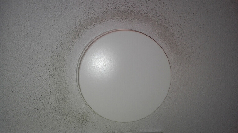 Round, white ceiling light with diffused cover on a textured ceiling.