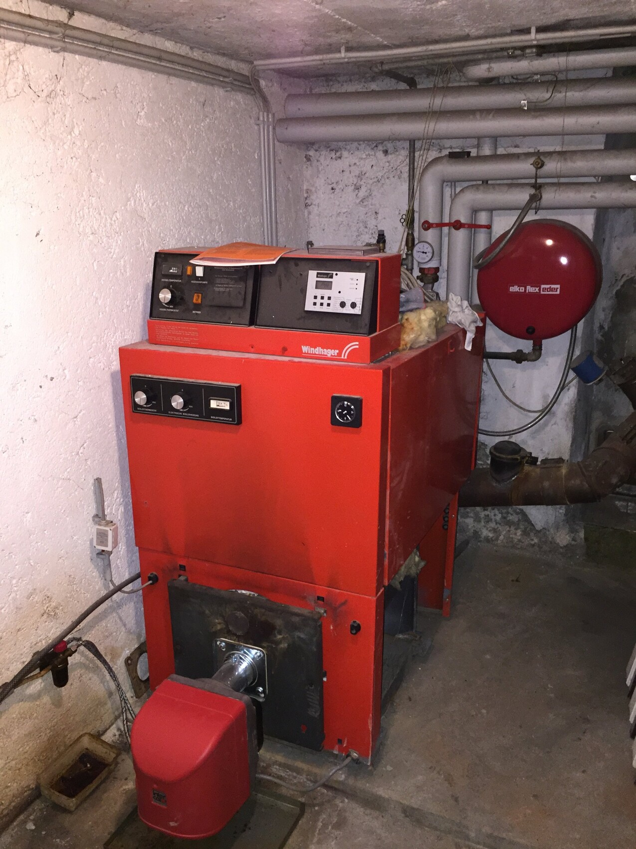 Red boiler in the basement with pipes, hot water system and measuring device.