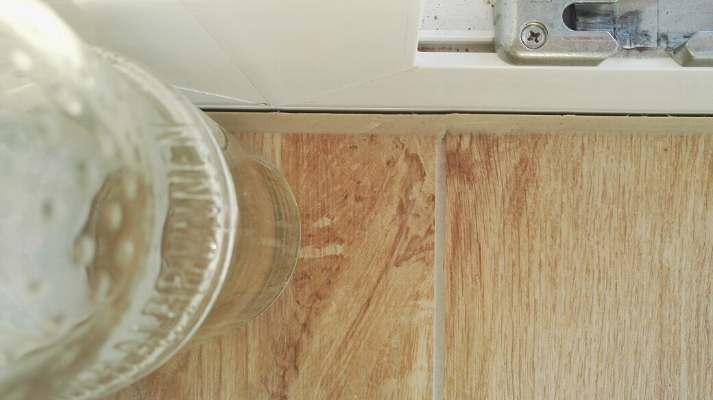 Close-up of a wood-look floor tile next to the door hinge and glass jug