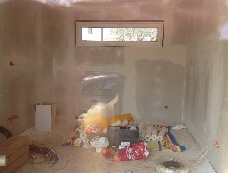 Renovierungsraum mit Baumaterialien, Kleingeräten und Kabeln; Fenster zeigt Auto draußen.