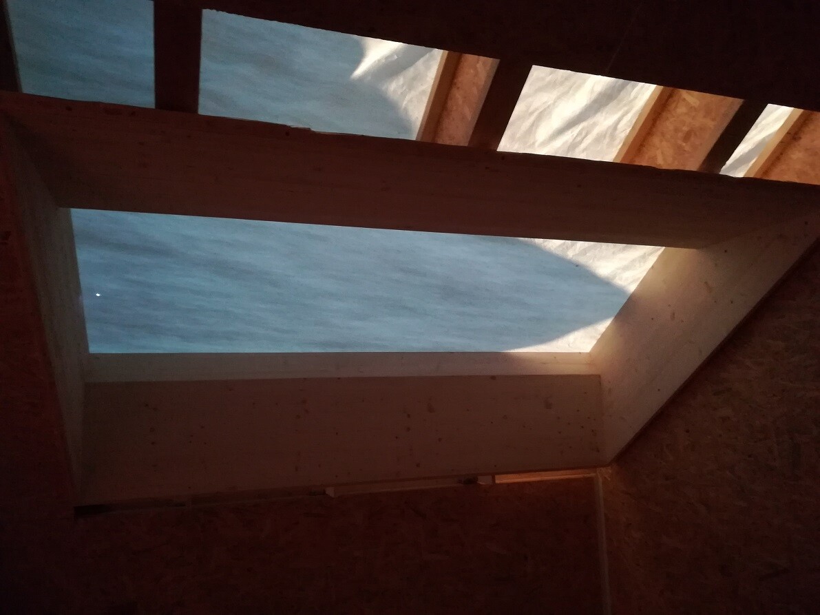 Open wooden roof truss in shell construction with light shining through a roof opening