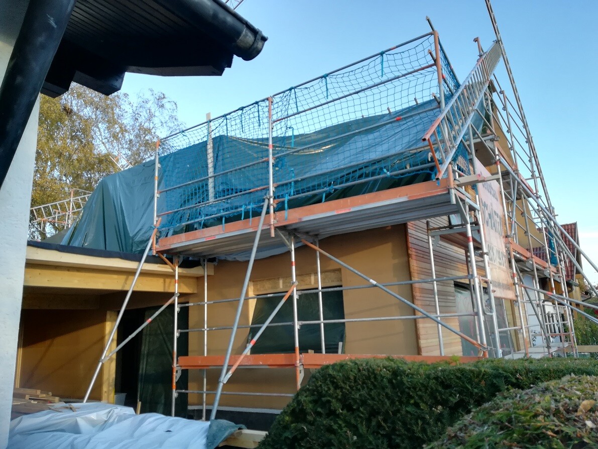 Construction site at the house with scaffolding, blue cover, and protective nets around the roof area