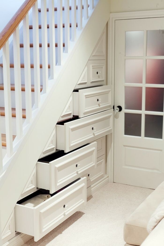 Under the stairs are several white drawers, next to them a glass door.
