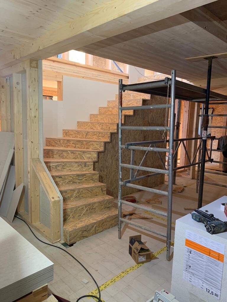 Construction site interior with wooden staircase made of OSB boards, scaffolding, and building materials