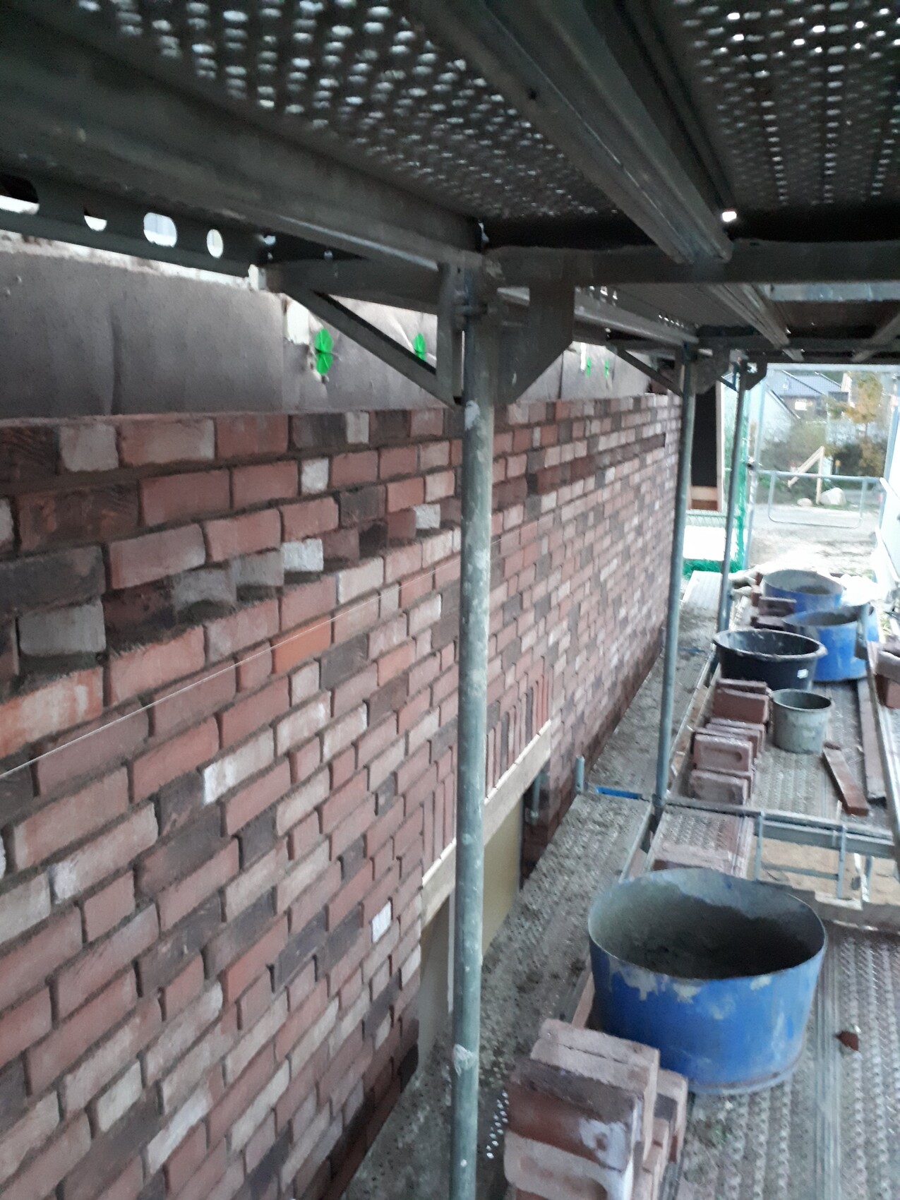 Red brick wall under scaffolding at the shell stage with construction equipment
