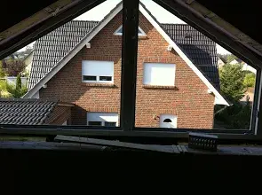 Blick aus einem Dachgeschossfenster auf ein rotes Ziegelhaus mit Satteldach.