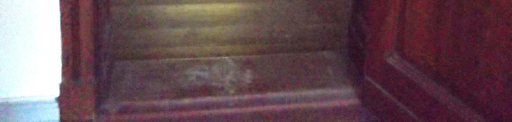 Dark wooden staircase from below, red wall on the right, light wall on the left.