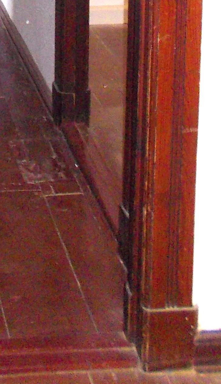 Interior corner with dark wooden wall, right wooden door frame, brown floor.