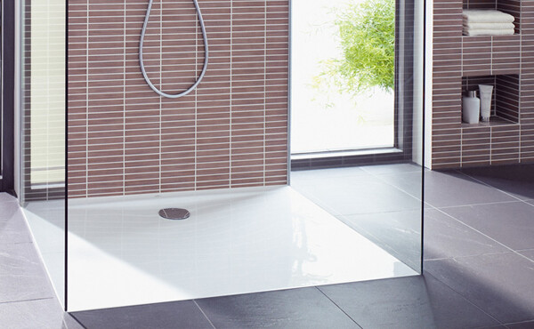 Modern shower area in the bathroom with glass partition, gray tiles, and showerhead.