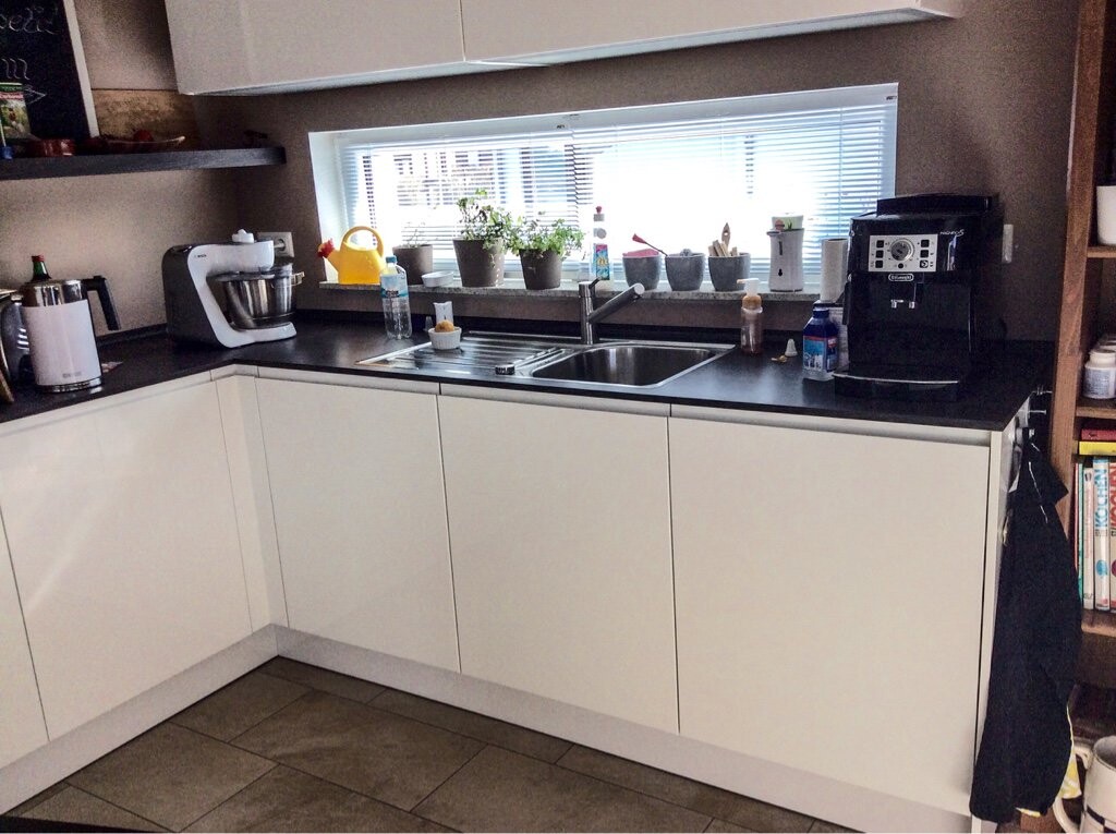 Modern kitchen with white cabinets, sink, coffee machine, and window.