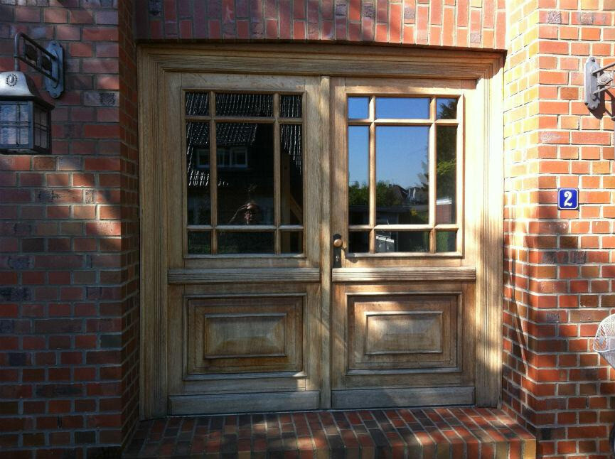 Double wooden doors opened in front of a red brick wall with glass windows