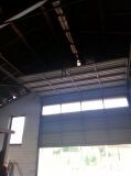Interior view of an unfinished garage shell with a large door area and visible ceiling beams.