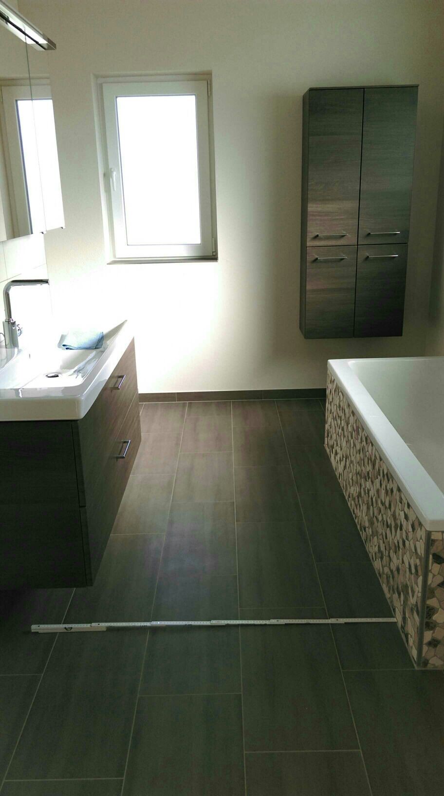 Bathroom with dark floor tiles, washbasin, wall cabinet, and bathtub.