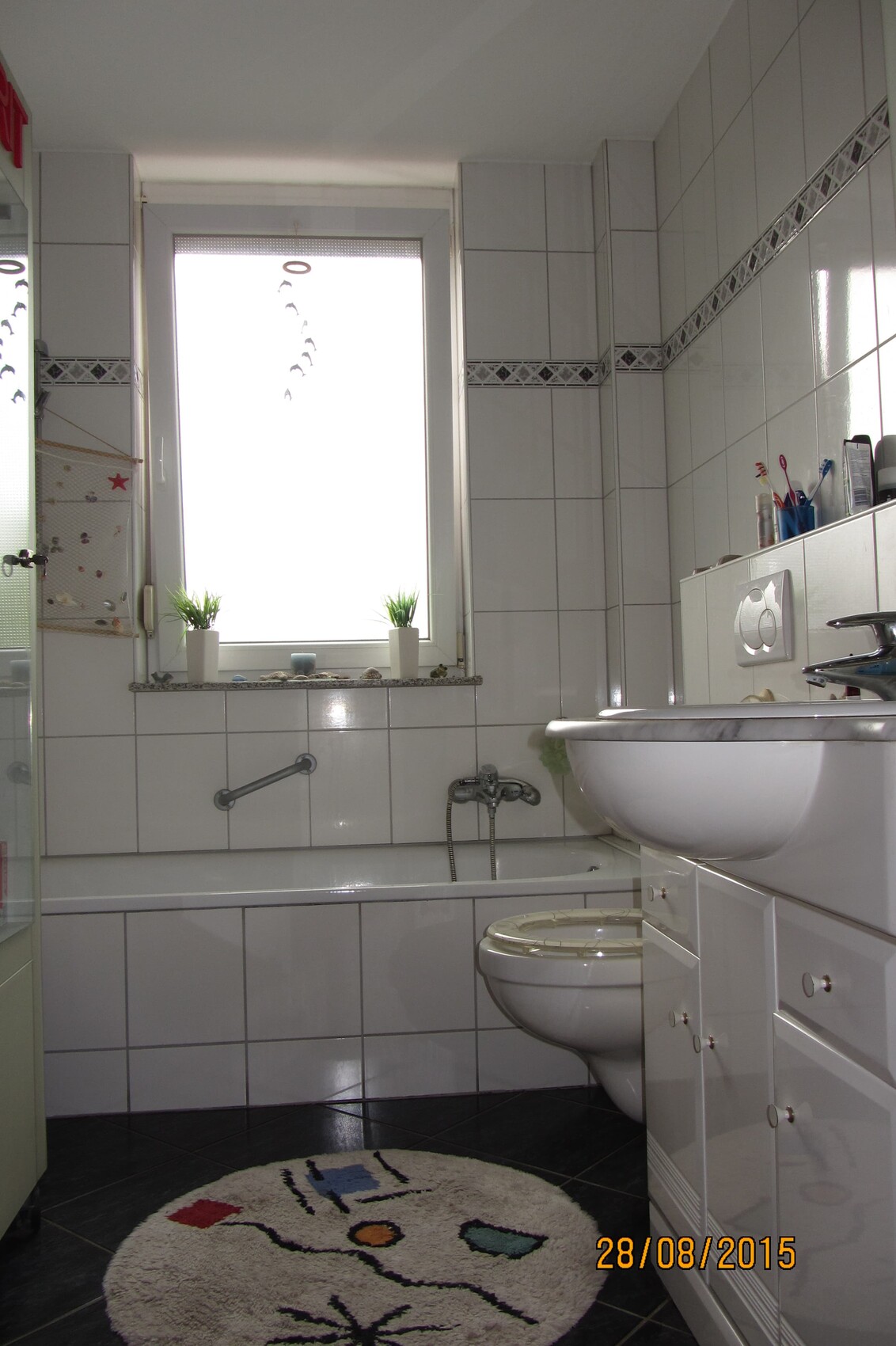 Bright bathroom with bathtub, toilet, sink, window, and decorative rug.