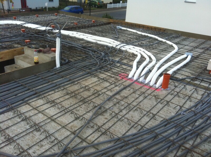 Baustellendach mit Bewehrungsstahlgitter, weißen Rohren und schwarzen Kabeln auf Betonboden