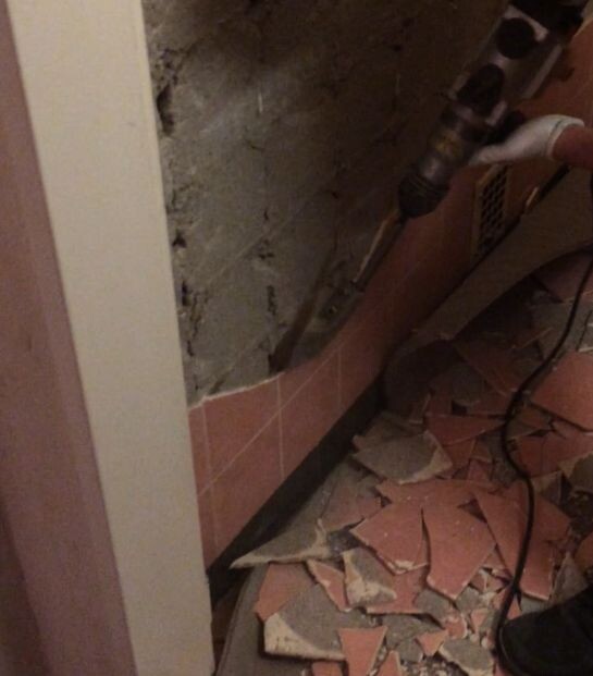 Bathroom construction site with exposed wall, broken tiles, and loose cables.