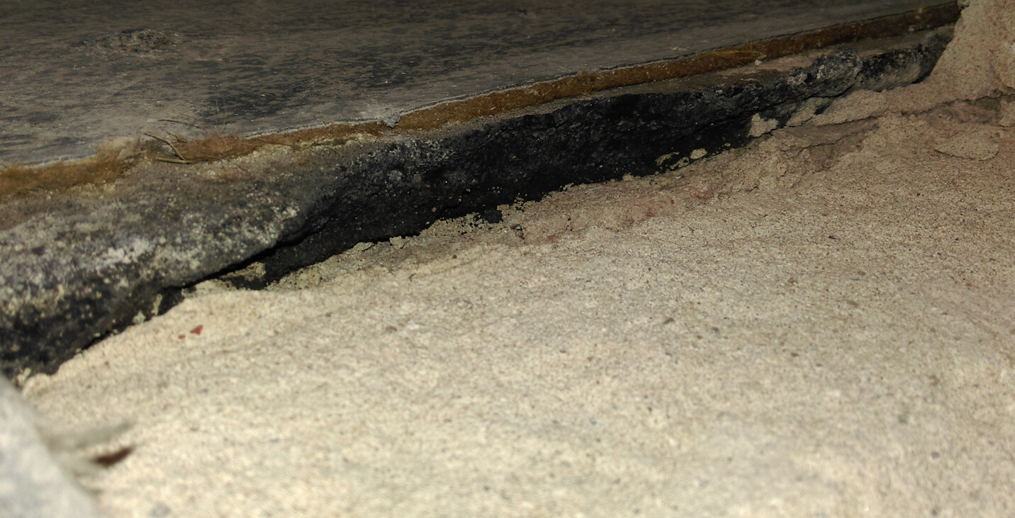 Close-up of a gap between concrete floor and wooden surface with dust and dark sealant.