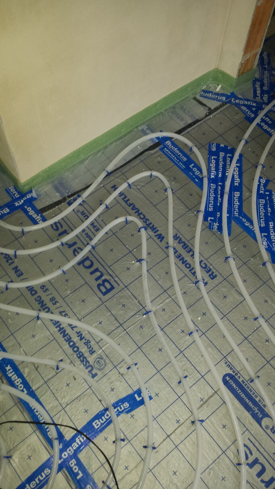 Underfloor heating: white pipes in loops on insulation foil with blue tape marking.