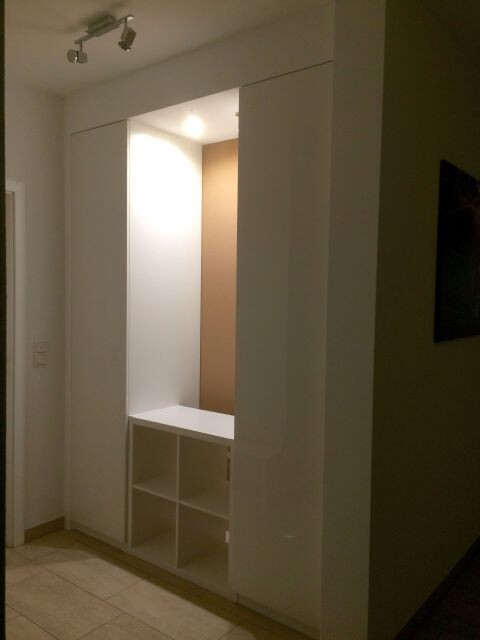 Modern white built-in wardrobe in the hallway with open cube compartments at the bottom and lighting.