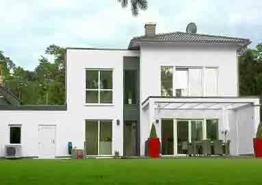 Modern white house facade with terrace, glass front, and green lawn.