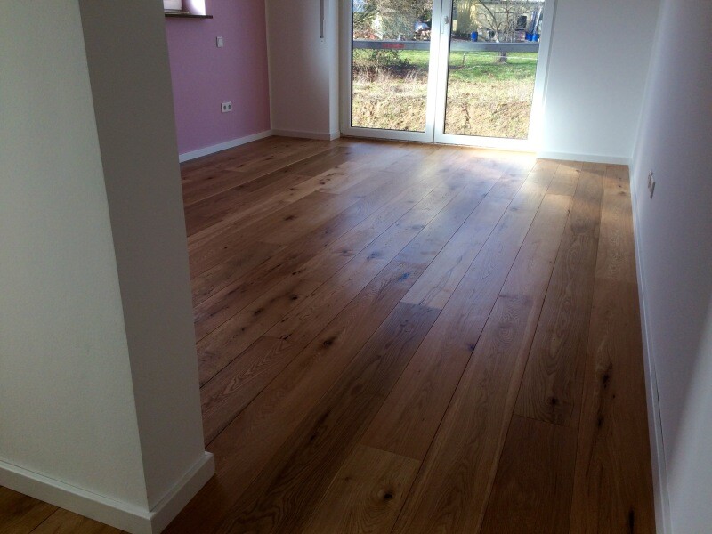 Empty living room with wooden floor, pink wall on the left, white walls, and large glass windows at the far end.