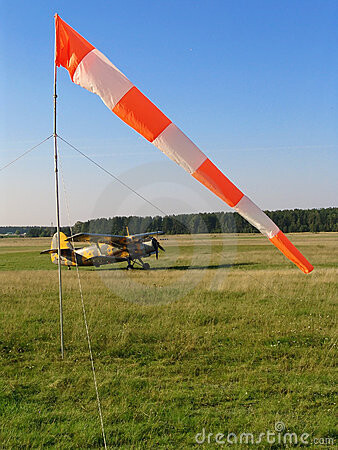 Windsock at an airfield with a small yellow airplane on grass runway