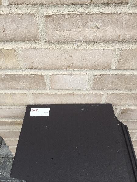 Black folder/case lying on the floor in front of brick wall; small white label.