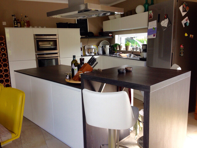 Modern kitchen with island, white cabinets, oven, and refrigerator.
