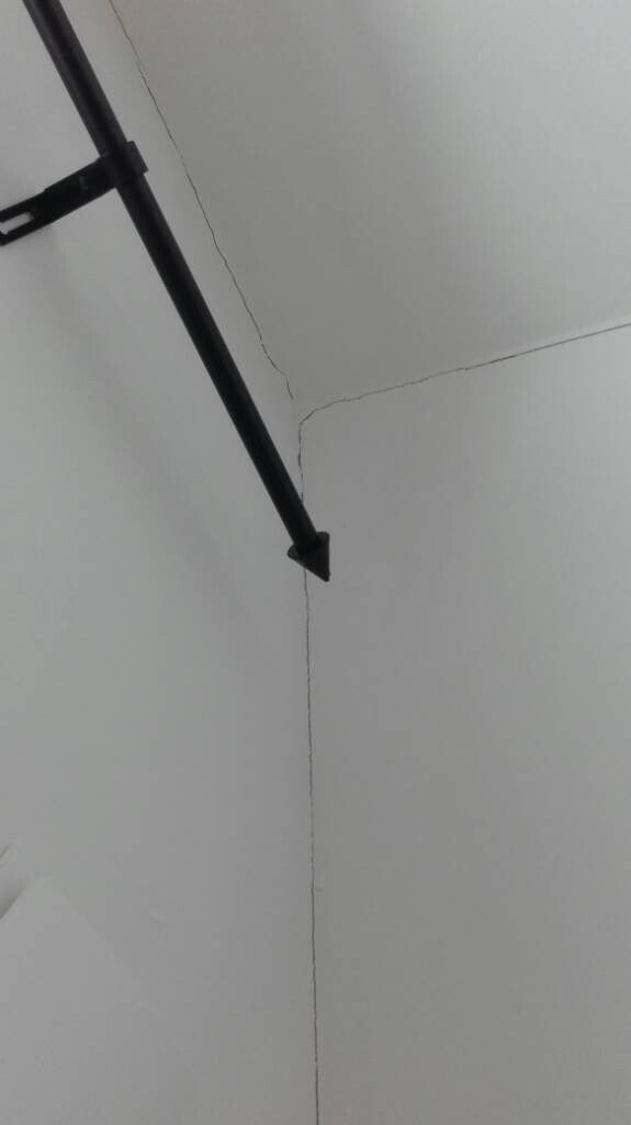 Corner of ceiling and wall with black rod; fine cracks visible.