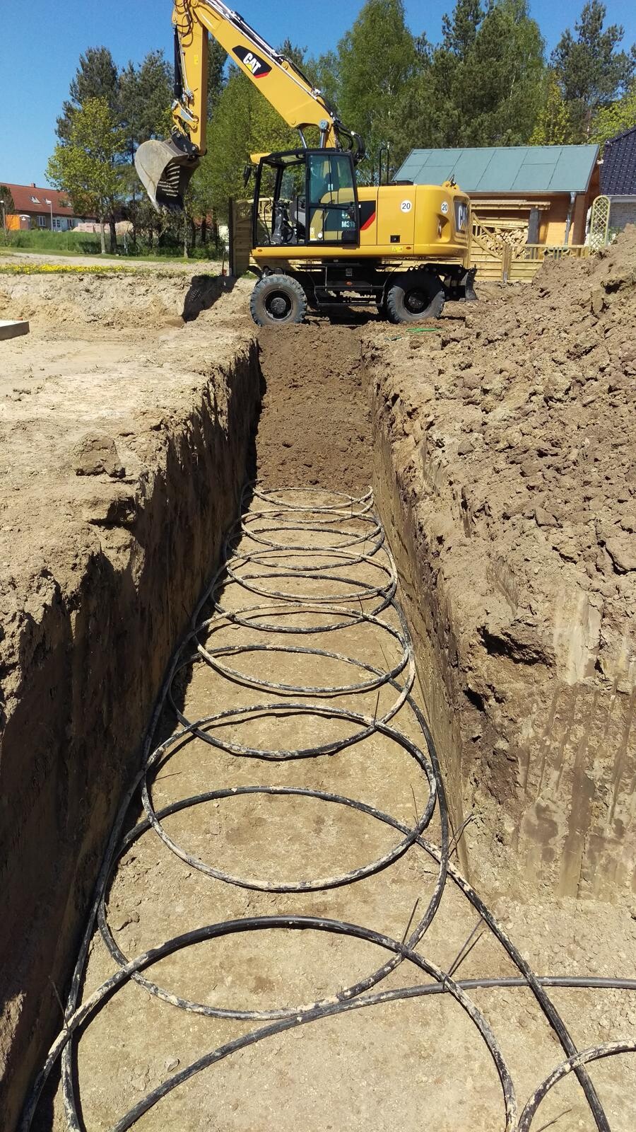 Yellow excavator stands over a construction pit; spiral reinforcement is lying on the bottom of the trench.