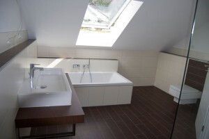 Bright modern bathroom with bathtub, washbasin, and glass shower under roof window.
