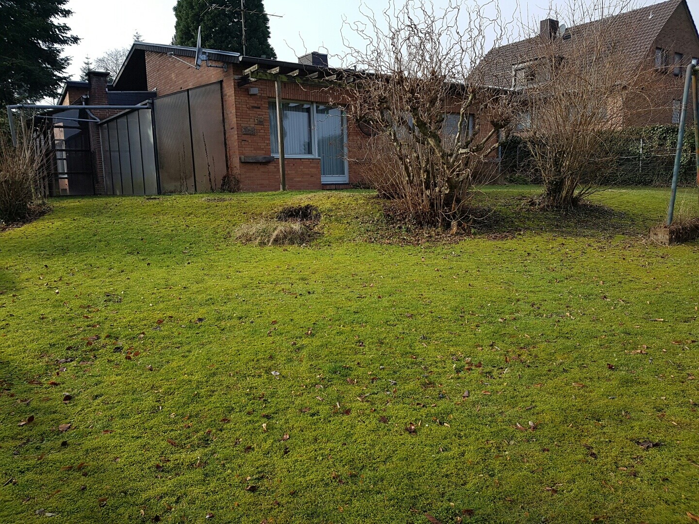 Garden with green lawn, shrubs, and a greenhouse next to the brown brick house.