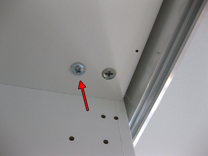 White furniture part with two screws, metal frame and drill holes.