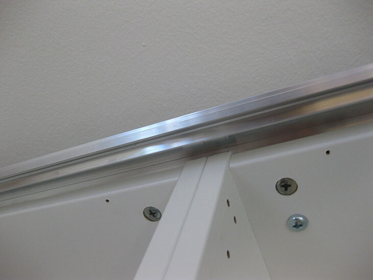 Close-up of white kitchen cabinet edge with metal profile and screws