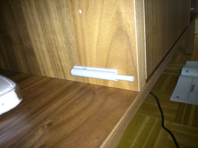 Small white plastic clip on the underside of a wooden cabinet, with a cable next to it.