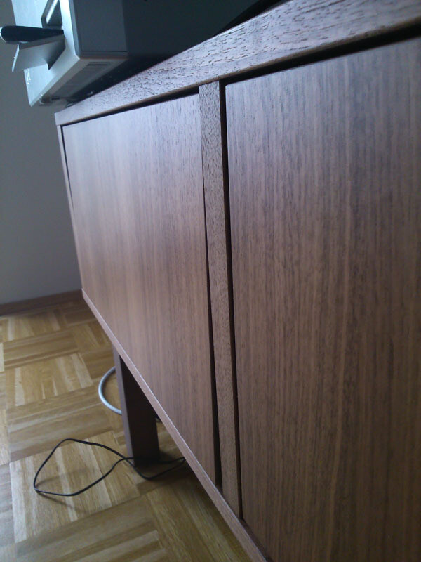 Close-up of a wood-finish base cabinet in an open-plan kitchen, cable on the floor