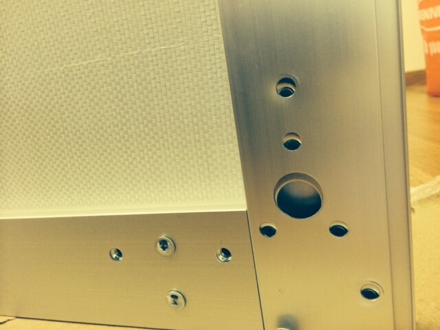 Close-up of a metal plate with screws and round openings, presumably a speaker cabinet.