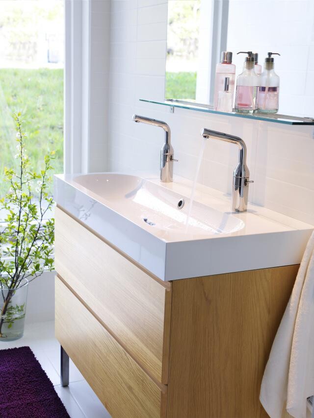 Modern vanity with two faucets, glass shelf, soap dispensers, and wooden base cabinet