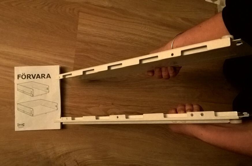 Person holding a white extendable shelf frame with rails, next to FÖRVARA instructions.
