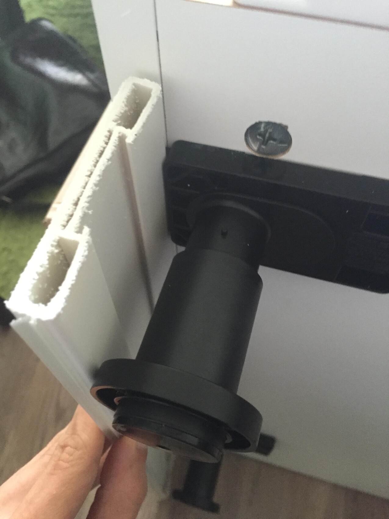 Close-up of a black plastic hinge arm on a white front panel, screw visible.