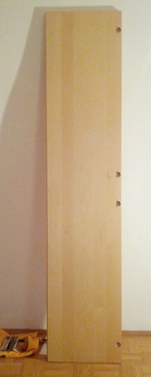 Vertically standing wooden panel with drill holes on the edge inside.