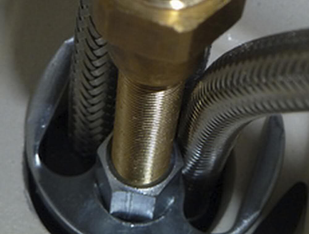 Close-up of a gold-colored threaded part in a mechanical fitting, surrounded by black brackets