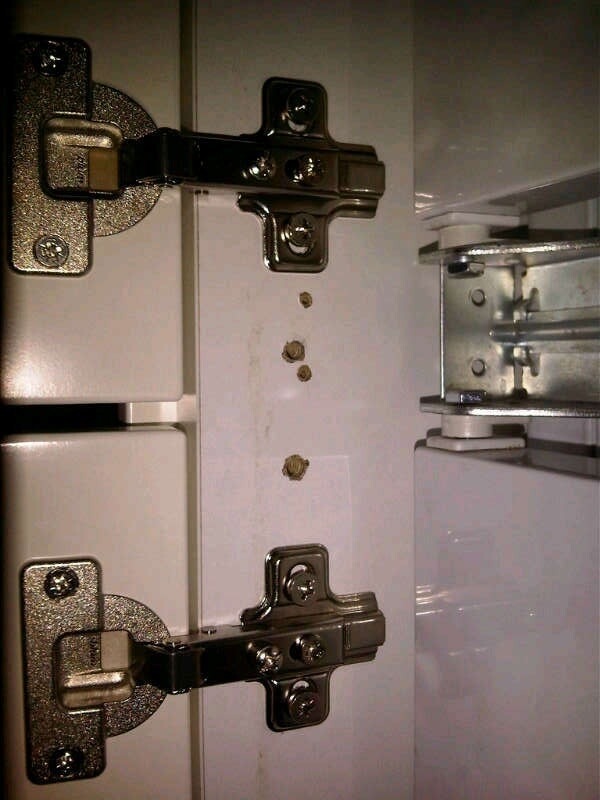 Close-up of metal hinges on a white kitchen cabinet door