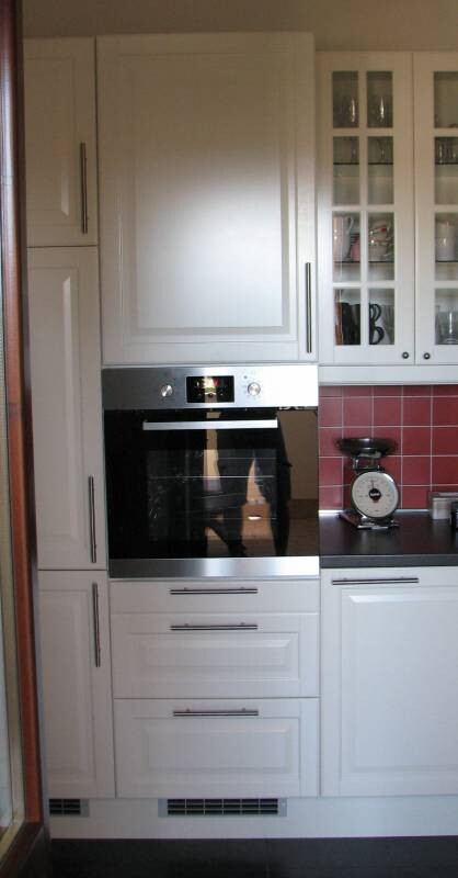 White kitchen unit with built-in oven, glass display cabinets and red tiled backsplash