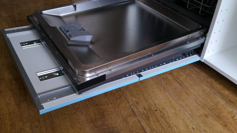 Pull-out kitchen drawer with metal tray and guide rails on wooden floor.