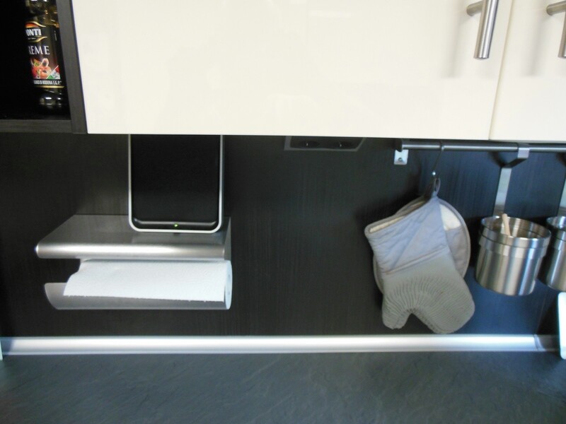 Under the kitchen cabinet: paper towel roll on the holder, oven mitt hanging, metal container to the right.