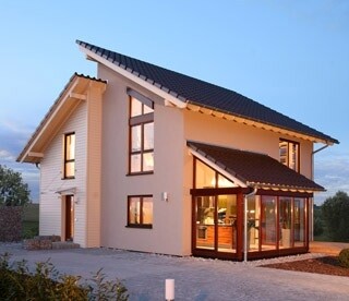 Two-story modern house with large conservatory and illuminated facade in evening light
