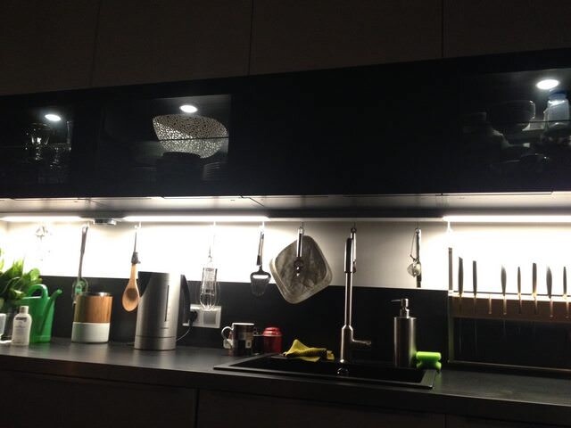 Modern kitchen: dark cabinets, under-cabinet lighting, hanging utensils above the sink.
