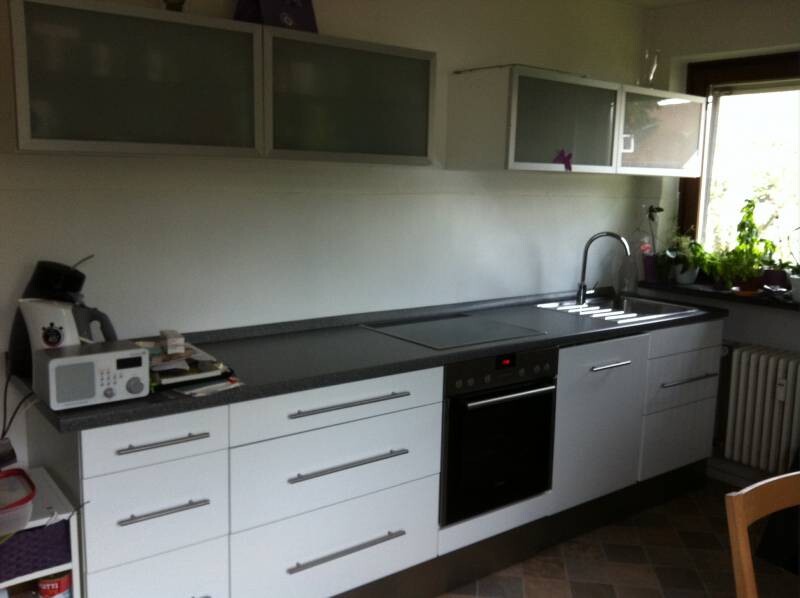 Modern kitchen with white fronts, dark countertop, sink and oven.