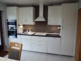 Kitchen with white fronts, countertop, range hood, and built-in oven.
